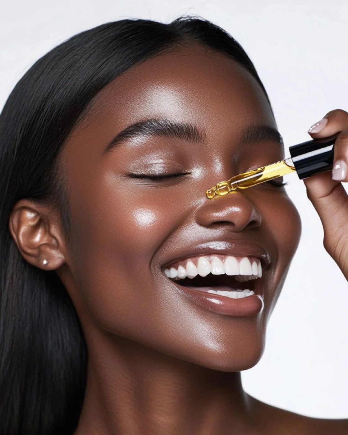 A woman with radiant, melanin-rich skin smiling as she applies a few drops of facial serum.
