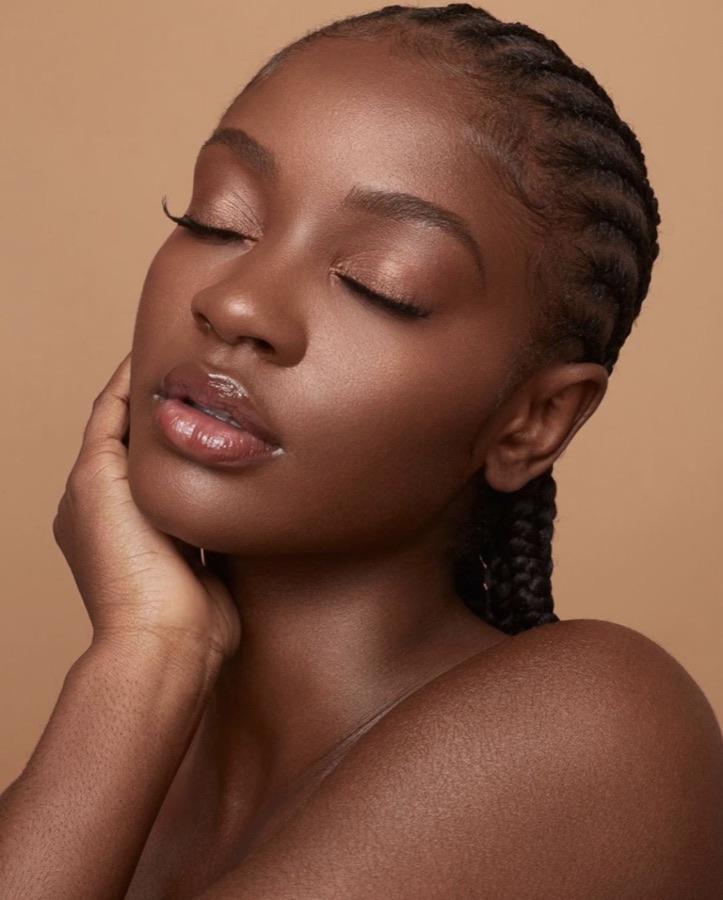 A woman with rich medium-deep skin and a luminous glow, eyes softly closed.