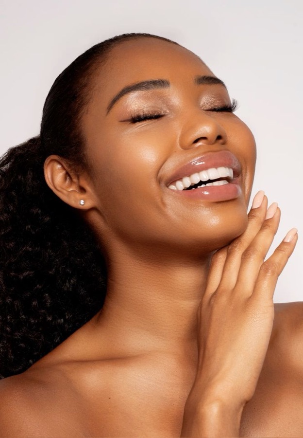 A woman with deep golden-brown skin laughing, skin radiant and healthy.